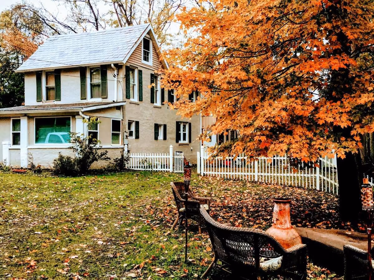 Frederick Cottage backyard with lawn, white picket fence, patio seating, and autumn trees