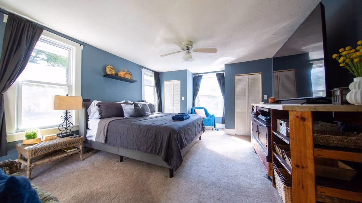 Frederick Cottage primary bedroom with king bed, blue walls, ceiling fan, and large TV
