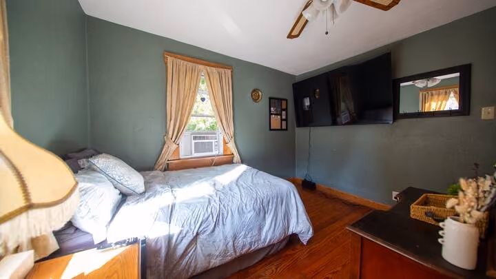Frederick Cottage second bedroom with bed, wall-mounted TV, wood floor, and window