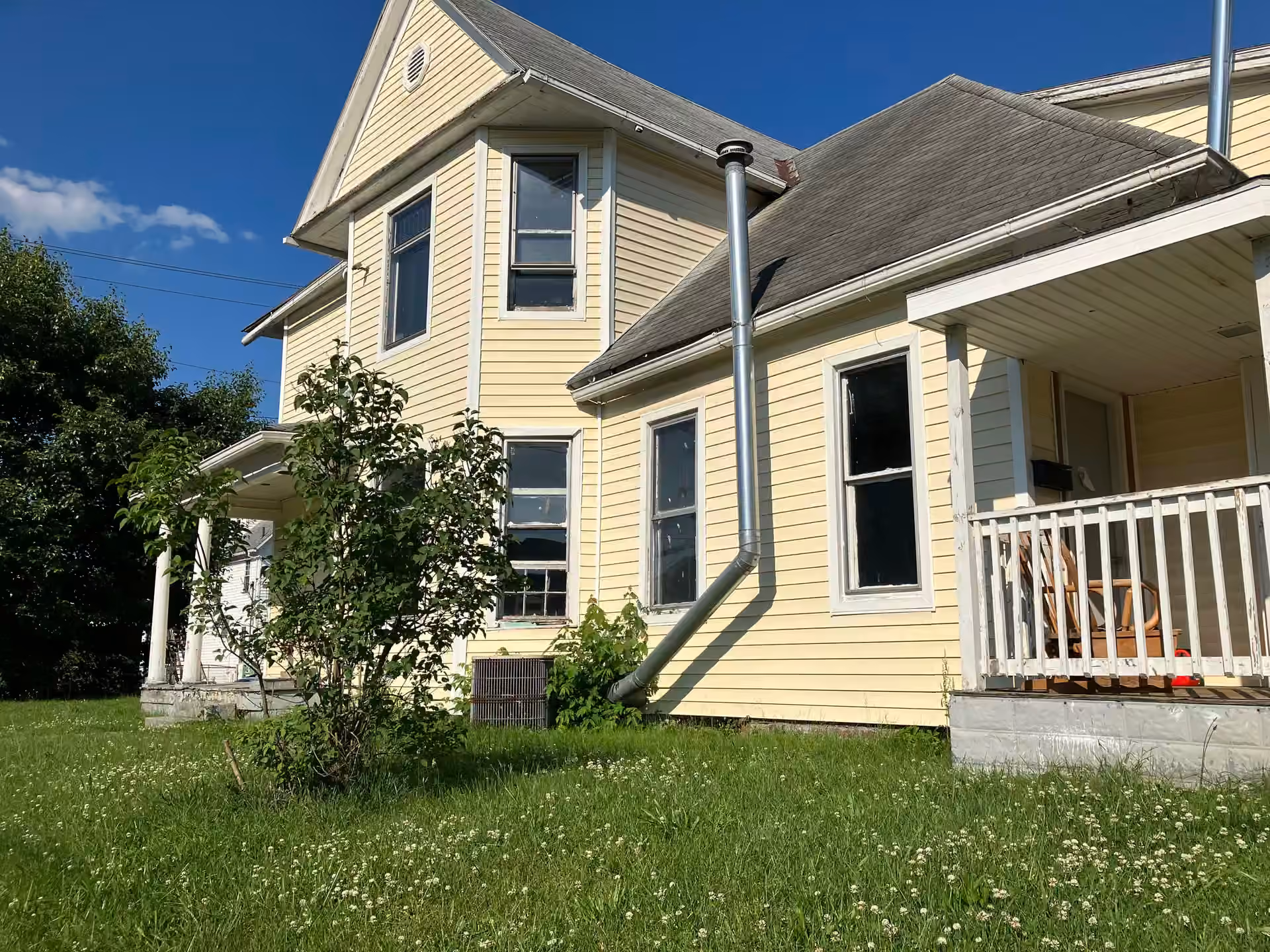 Yellow Cottage exterior with porch, pale siding, windows, and blue sky